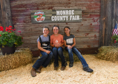 Three girls sitting on a hay bail at the Monroe County Fair.