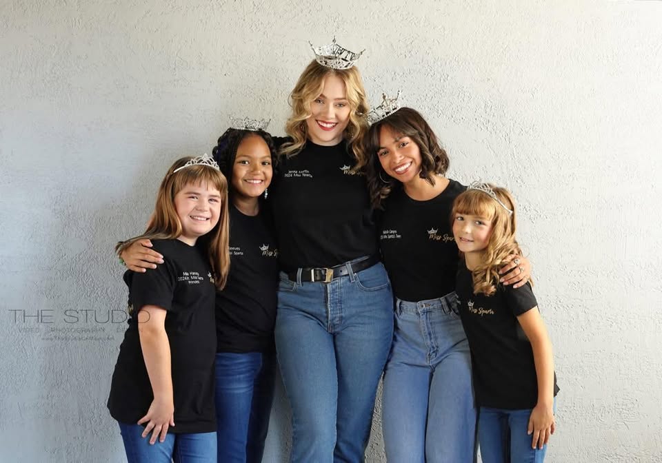 A young woman and girls smile together in tiaras.