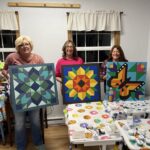 three women hold their barn quilt creations