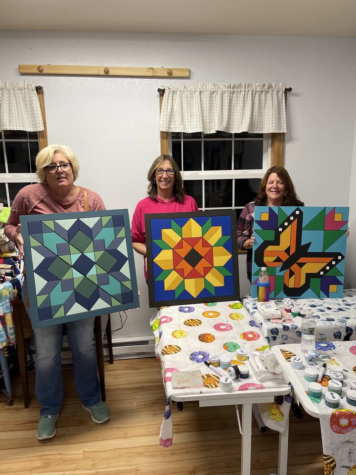 three women hold their barn quilt creations