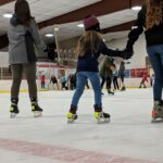 A child ice skating in an arena while holding an adults hand