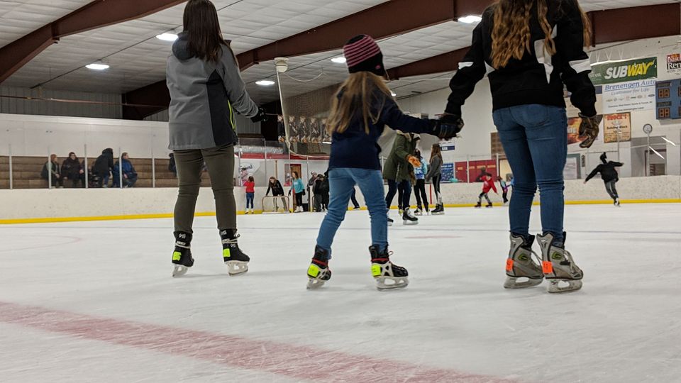 A child ice skating in an arena while holding an adults hand