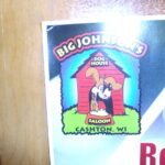 A poster with a picture of a dog in a doghouse sitting behind a bowl of dog food.