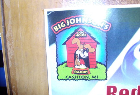 A poster with a picture of a dog in a doghouse sitting behind a bowl of dog food.