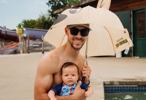 A picture of a man with a beard smiles while holding a baby