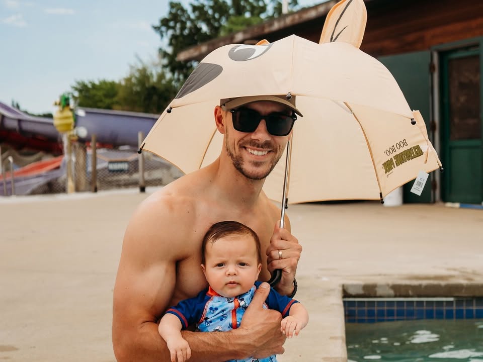 A picture of a man with a beard smiles while holding a baby