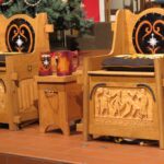 Two ornate wooden thrones with high backs, featuring black velvet cushions embroidered with golden designs