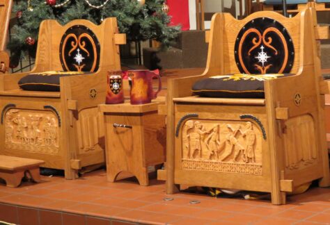 Two ornate wooden thrones with high backs, featuring black velvet cushions embroidered with golden designs