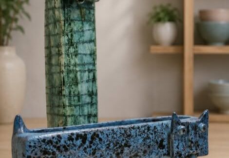A tall thin vase with a cat face and a short wide planter with a cat face.