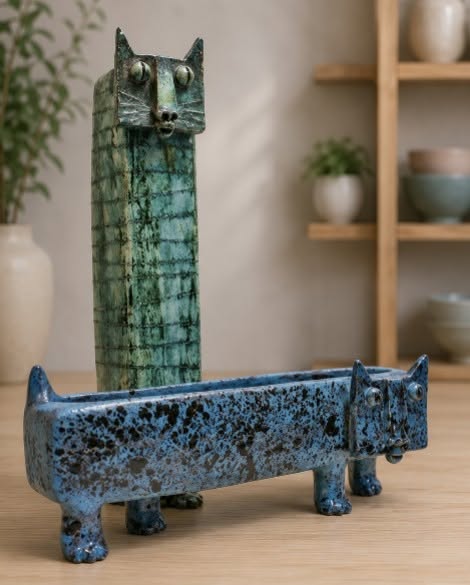 A tall thin vase with a cat face and a short wide planter with a cat face.