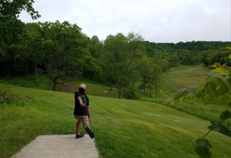 A man throws a disc golf from atop a hill