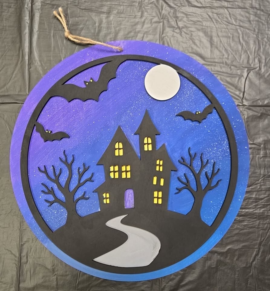 A painted circular door hang with a spooky house and bats.